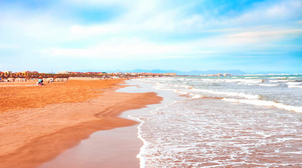 Hermosa playa de valencia donde se ve la gran costa intermable y el mar azul rompiendo en la orilla